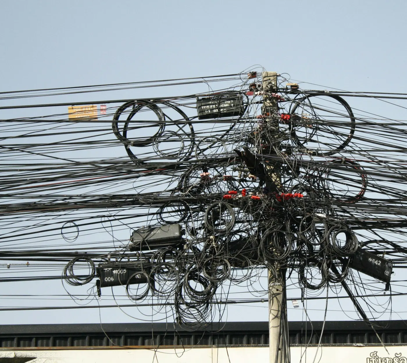 A telephone pole completely overrun with a tangled mass of black cables, loops and junction boxes — a chaotic web of wires